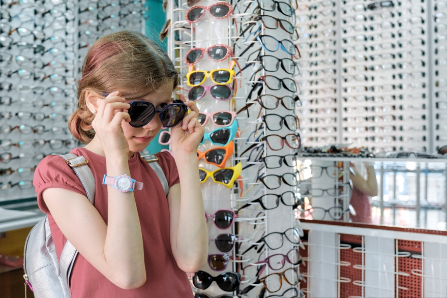 Girl looking and choosing sunglasses at local optician